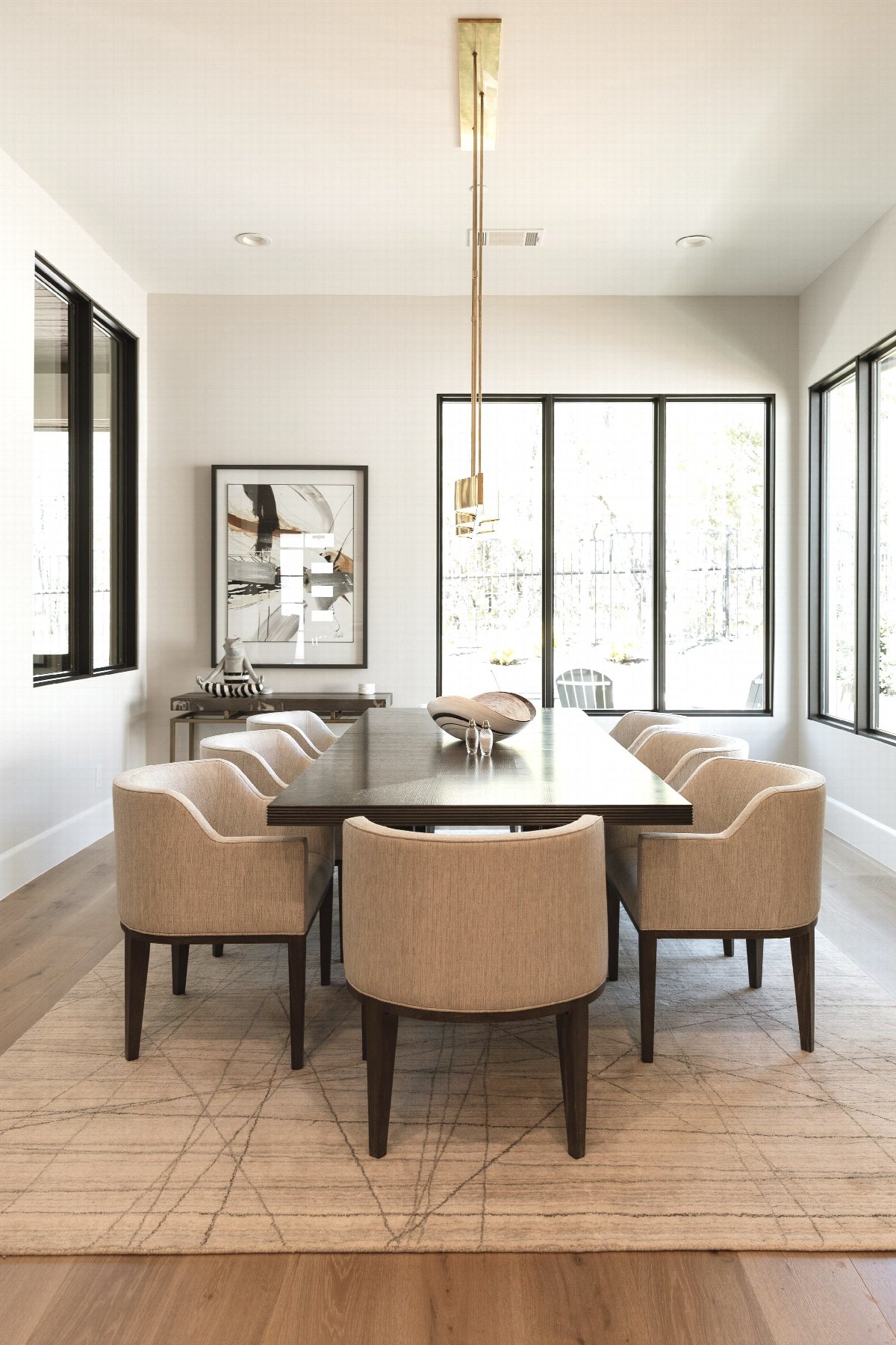 Modern dining room with rectangular wood table, upholstered chairs, pendant lighting, and large windows in a bright, minimalist interior design.