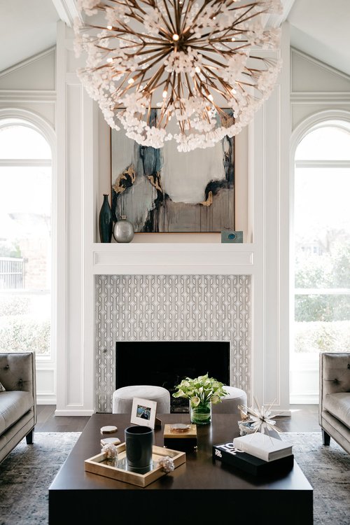 Luxury living room with statement chandelier, fireplace, custom millwork, and modern coffee table in a bright, elegant interior.