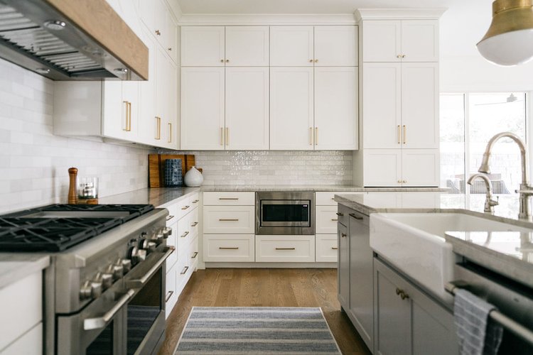 Luxury white kitchen design with custom cabinetry, marble countertops, farmhouse sink, and stainless steel appliances in a bright, modern interior.