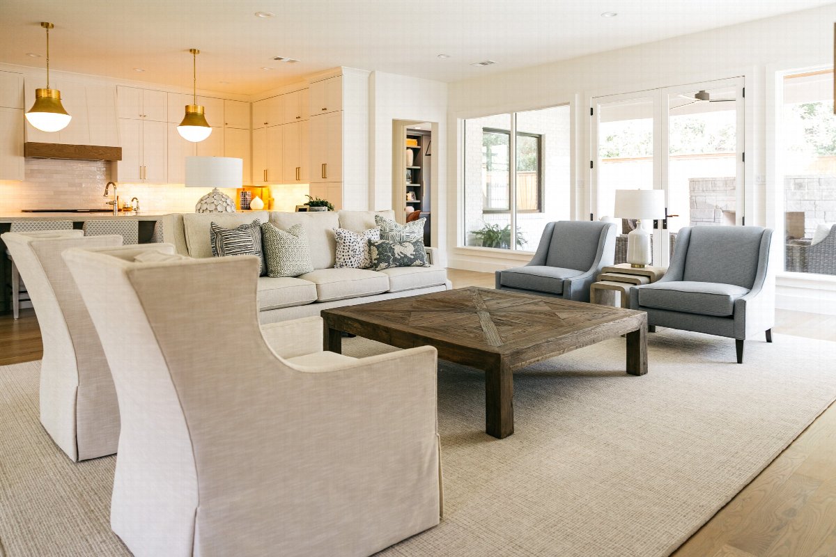 Open-concept living room and kitchen with neutral furniture, wood coffee table, custom cabinetry, and large windows in a bright, modern home.