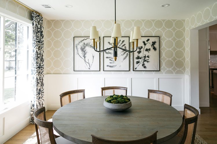 Elegant dining room with round wood table, upholstered chairs, chandelier, and patterned wallpaper in a bright, transitional interior design.