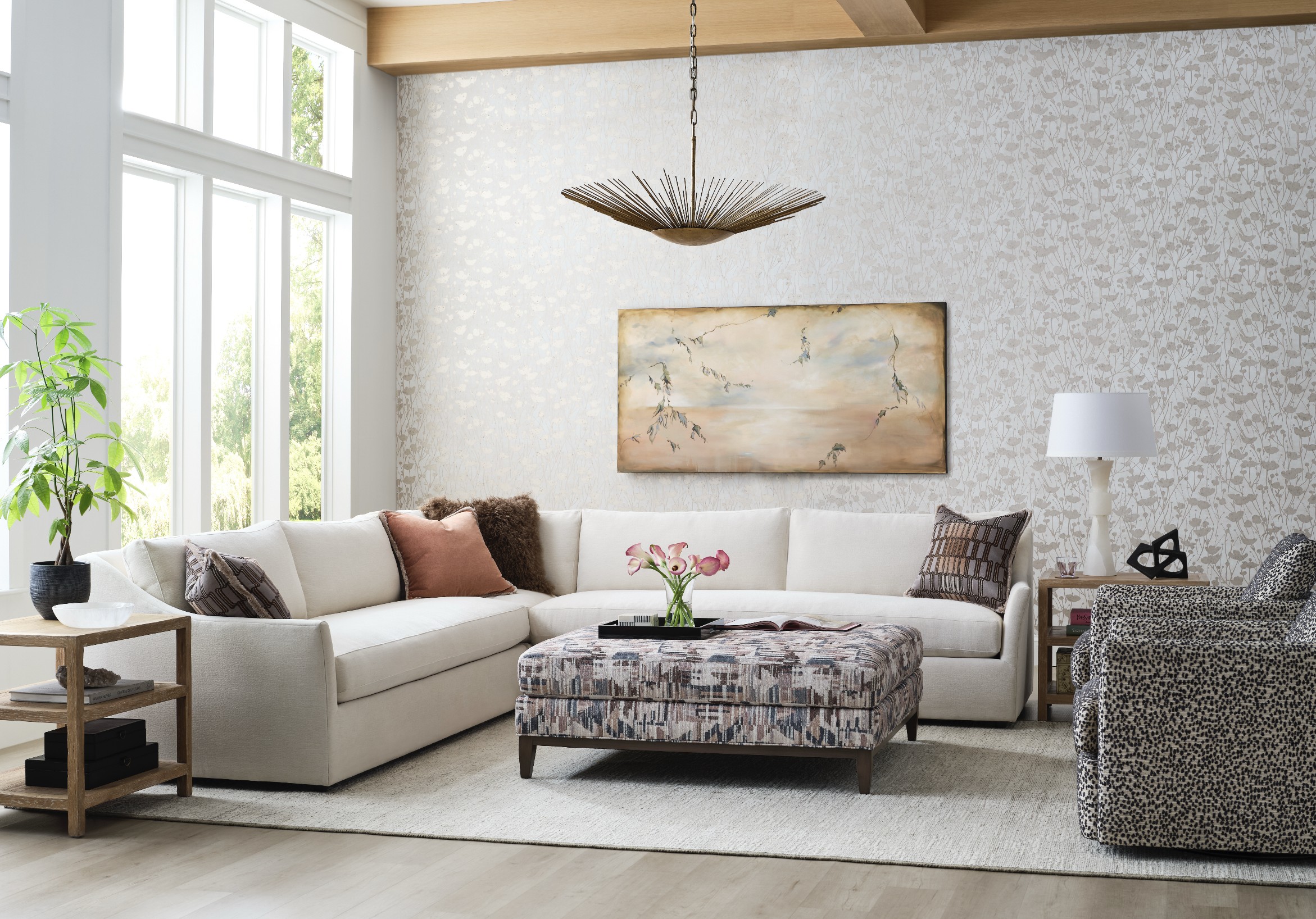 Luxury living room with sectional sofa, upholstered ottoman, designer lighting, and large windows in a bright, modern interior design.